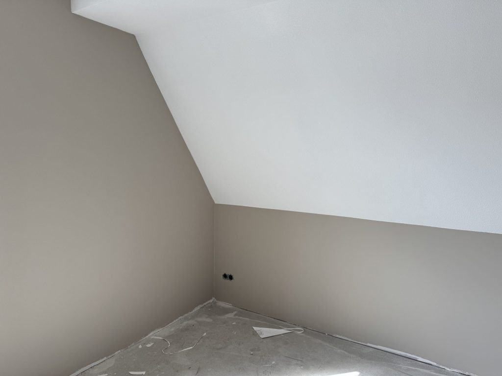 Zolderkamer met een strak wit schuin plafond boven een lichte wand