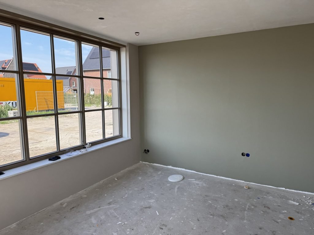 Egaal afgewerkte wand in een grijsgroene tint naast een groot raam in een nieuwbouwkamer