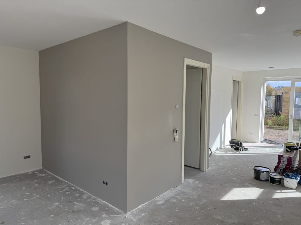 Pas gesausde grijze wand met verfemmers en een roller op de vloer