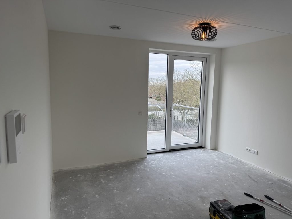 Lege kamer met strak afgewerkte witte wanden en openslaande deuren